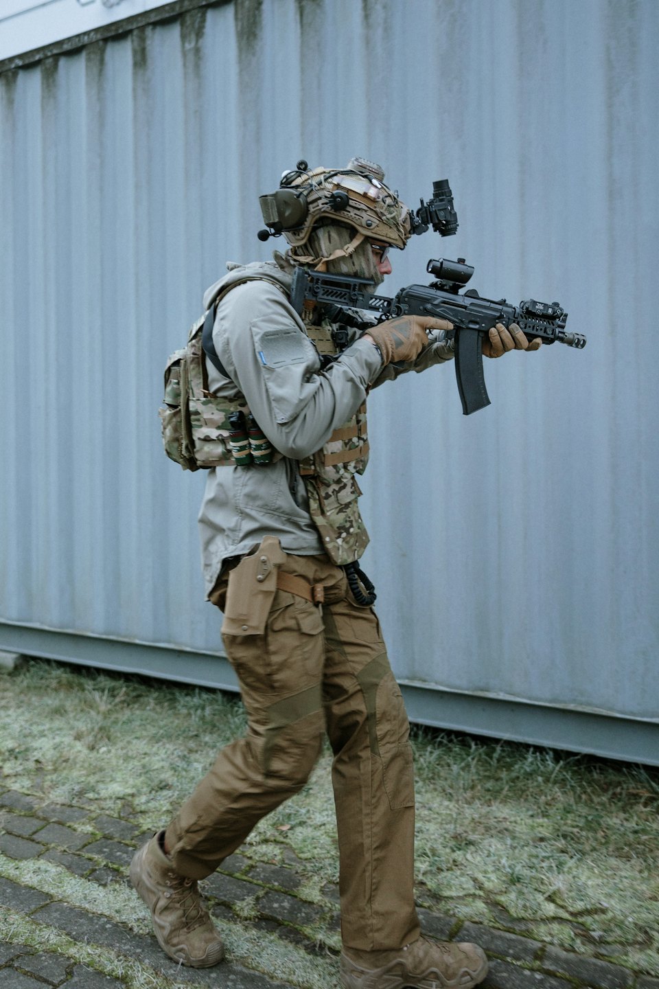 Ein Soldat in Kampfausrüstung geht an einer Wellblechwand vorbei.